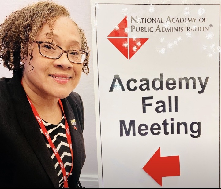 NASPAA Immediate Past President RaJade Berry-James standing next to a sign with the NAPA logo the words "Academy Fall Meeting" and a red arrow